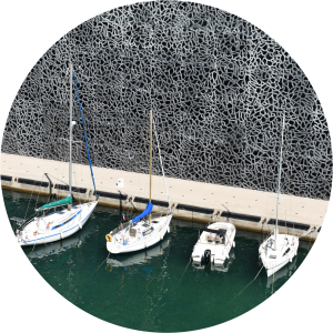 Decorative image of a row of boats in a harbor against a wall with lacy stainless steel designs.